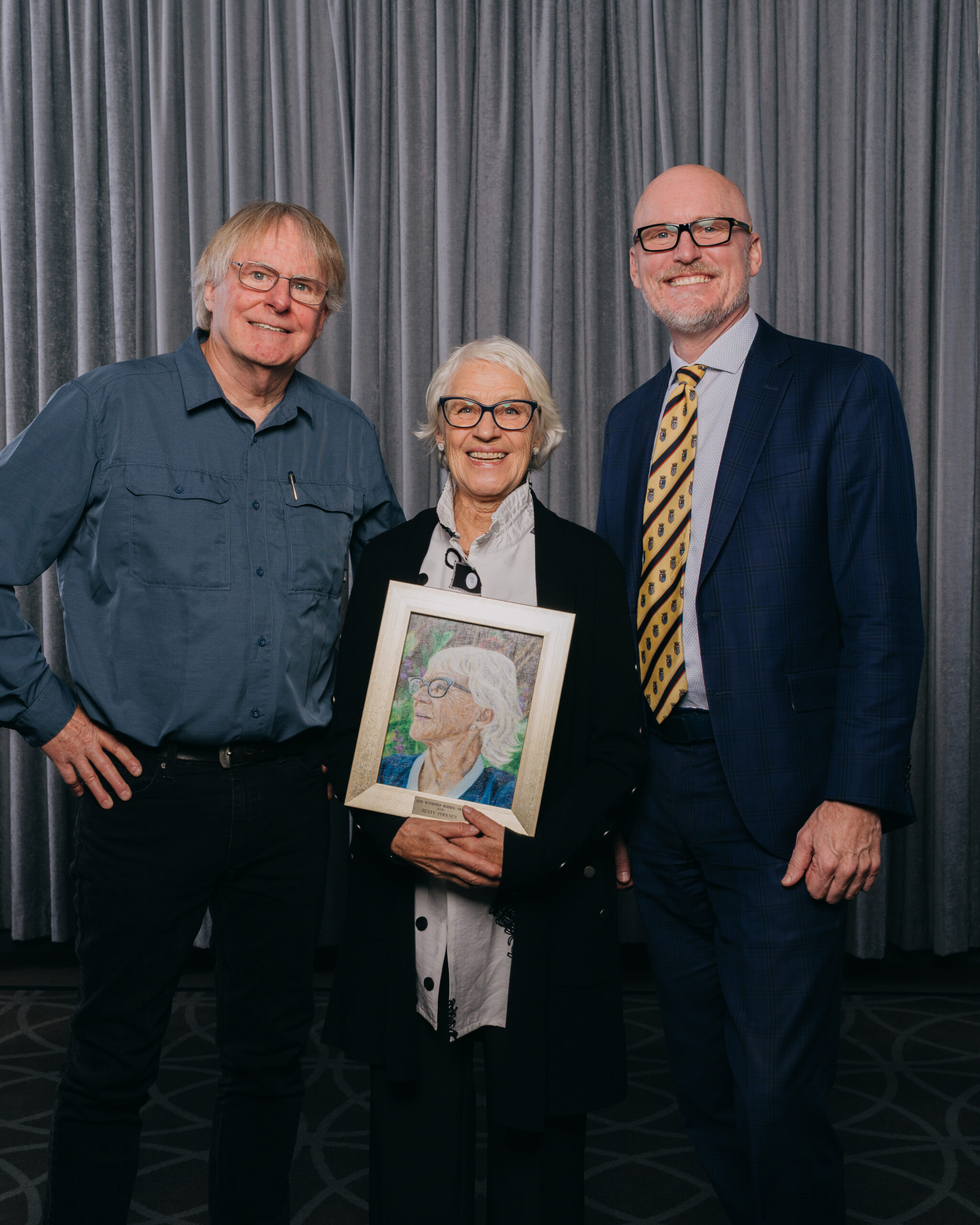 AAC President Jon Oxley, Joan Waterfield Award recipient Betty Poulsen (holding her portrait) and Mayor Blaine Hyggen.  Photograph by Angeline Simon for the AAC 2026.